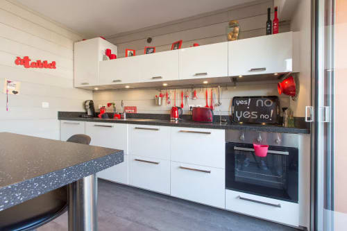 Cuisine moderne à Zoppas Aix-les-Bains avec armoires blanches, plan de travail foncé, accents rouges et appareils inox