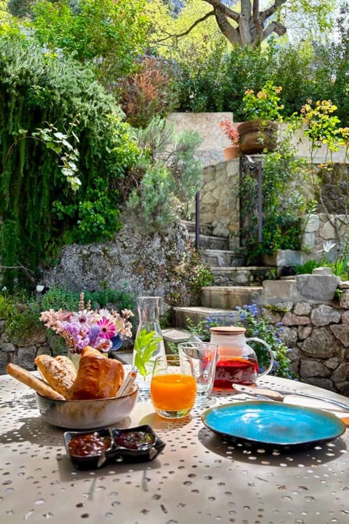 Frühstückstisch in der La Bouscatière B&B in Moustiers-Sainte-Marie mit frischem Brot, Blumen, Saft und blauem Teller
