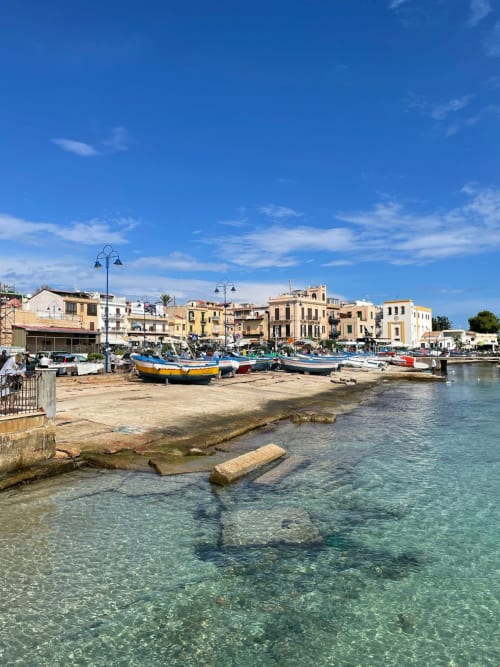 Mondello Beach harbor with colorful fishing boats and traditional Palermo waterfront architecture under blue sky