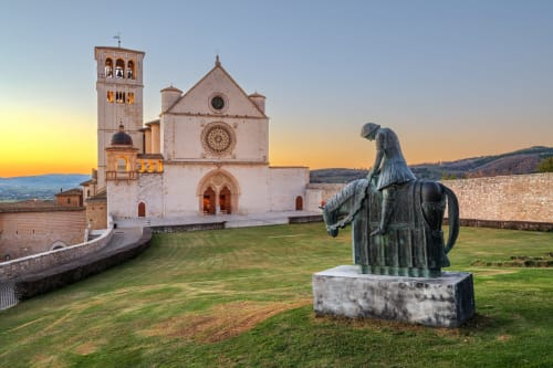 Statua in bronzo che domina la Basilica di San Francesco al tramonto ad Assisi, Italia