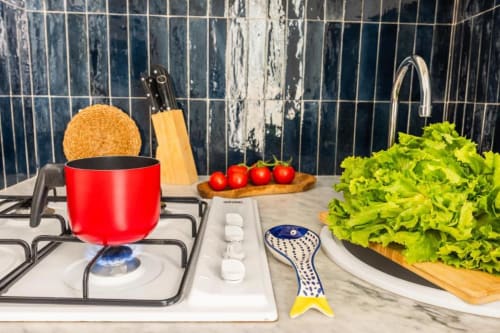Modern kitchen setup at Dimora Silva with red pot, fresh lettuce and tomatoes on marble counter, blue tiled backsplash.
