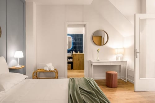 Bright bedroom at Dimora Silva Nature Suites with white bed, vanity desk, round mirror, and wooden flooring overlooking city