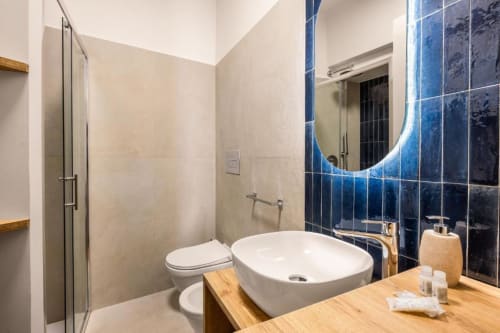 Modern bathroom at Dimora Silva with blue tile wall, round vessel sink, LED mirror, toilet, and walk-in shower enclosure