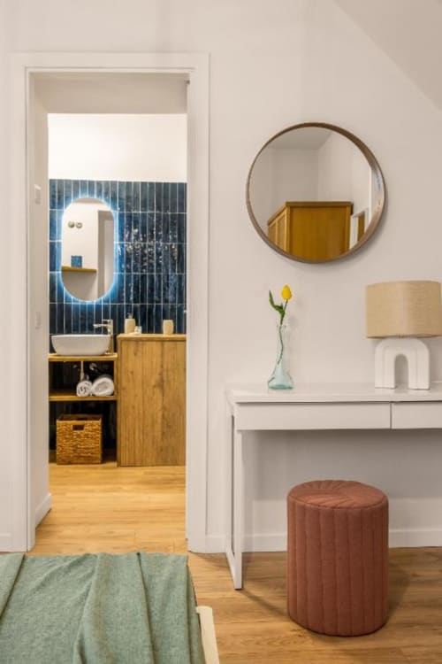 Modern apartment entryway with view into contemporary bathroom featuring blue tile wall, illuminated mirror, wooden vanity,