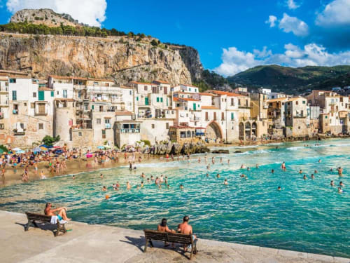 Mondello Beach with colorful historic buildings nestled against dramatic limestone cliffs under blue sky with turquoise