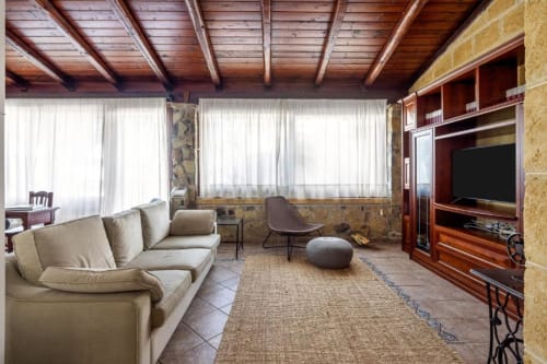 Spacious villa living room with wooden beams, beige sofa, terracotta floors, and large windows overlooking ocean views at