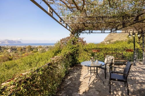 Terrace at Dimora Silva Nature Suites villa with dining table, chairs, pergola, and sea views of Palermo coastline