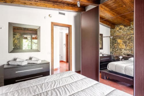 Modern villa bedroom with wooden beams, mirrored closet, and stone accent wall at Dimora Silva Nature Suites