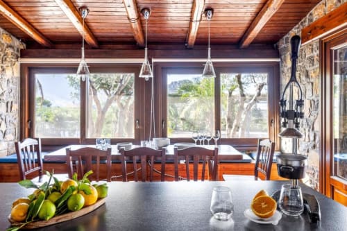 Modern villa dining room with wooden beams, stone walls, pendant lights, and panoramic windows overlooking Mediterranean