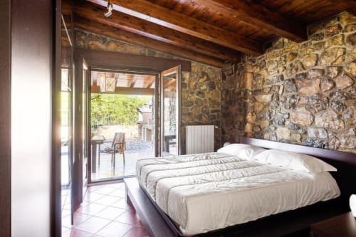 Bedroom in Dimora Silva Nature Suites villa with double bed, stone walls, wooden beams, and terrace access overlooking