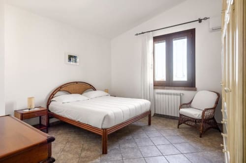 Bright bedroom at Dimora Silva Nature Suites villa with wooden bed, rattan chair, and mountain views through glass doors
