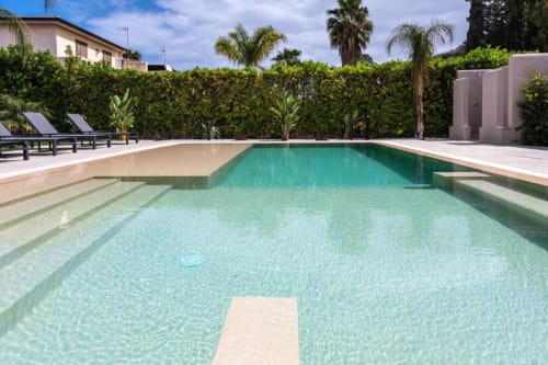Lussuosa piscina di Dimora Silva con acqua turchese, lettini, palme e siepi curate a San Martino delle