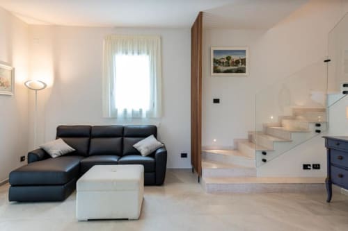 Zona living di villa moderna con divano in pelle nera, pouf bianco e scala presso Dimora Silva Nature Suites