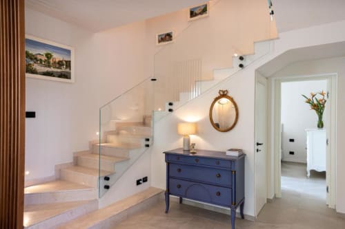 Ingresso di villa moderna con scala sospesa, ringhiera in vetro, cassettone blu e specchio presso Dimora Silva Nature Suites