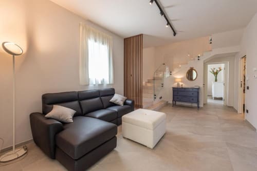 Soggiorno moderno della villa con divano in pelle nera, pouf color crema e ingresso doccia in vetro presso Dimora Silva Nature Suites