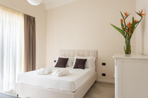 Camera da letto della villa moderna con biancheria bianca, cuscini scuri e fiori freschi presso Dimora Silva Nature Suites a San Martino delle