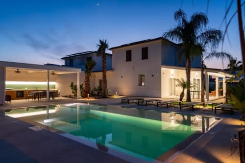 Villa moderna con piscina illuminata al tramonto, palme e terrazza presso Dimora Silva Nature Suites