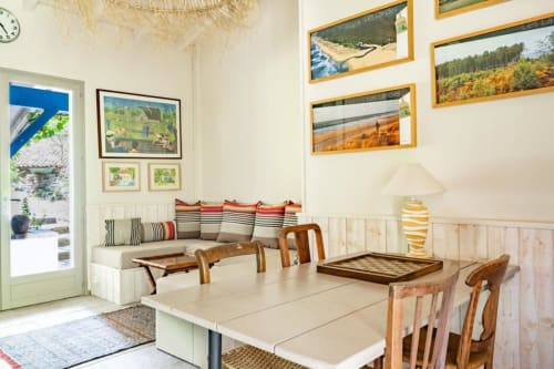 Salle à manger lumineuse du Moulin De Lassalle avec table en bois, photos de paysages encadrées et banquette à coussins rayés