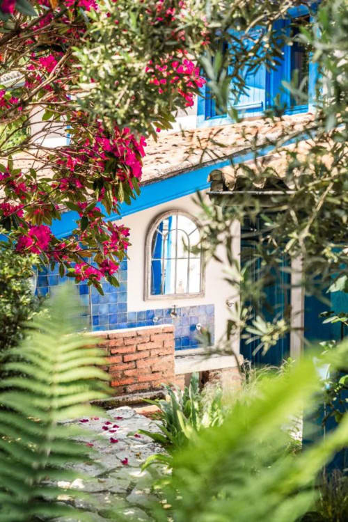 Les bougainvillées magenta éclatantes encadrent les volets bleus du Moulin De Lassalle, un charmant hôtel à Linxe, en France