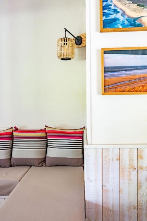 Chambre au charme balnéaire au Moulin De Lassalle avec coussins rayés, luminaire suspendu tressé et photographies de plage encadrées