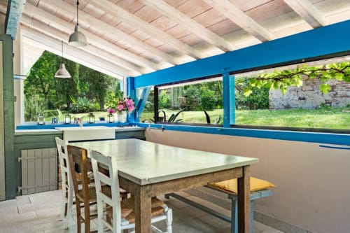 Chambre sud ensoleillée au Moulin de Lassalle avec table à manger, fenêtres à encadrements bleus donnant sur le jardin, poutres en bois
