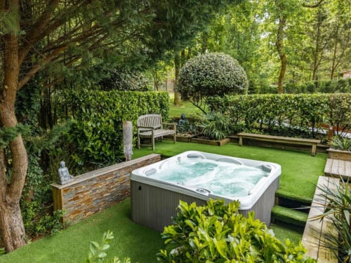 Baignoire à remous luxueuse dans le jardin paysagé du Moulin De Lassalle à Linxe, entourée de haies verdoyantes et de places assises