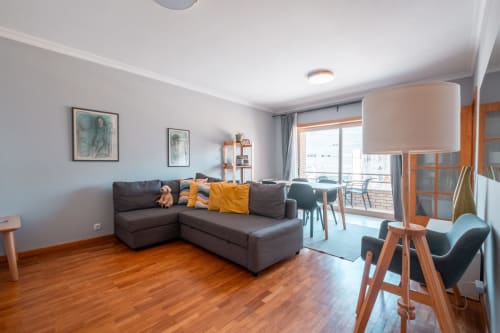 Modern apartment living room at EcoHost Perafita with gray sectional sofa, wooden floors, and balcony view