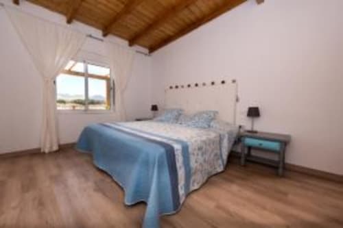 Habitación luminosa en Smart Rent Fuerteventura con ropa de cama azul, techo de madera y vistas a la montaña desde ventana grande