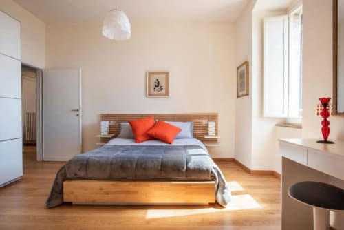 Camera moderna a Proprietà Clara ad Assisi con letto in legno, cuscini arancioni, finestra luminosa e arredamenti minimalisti