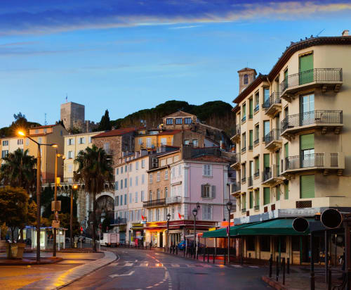 Scène de rue à Cannes au crépuscule avec bâtiments historiques, palmiers et architecture colorée près de l'hôtel Kimi Résidence