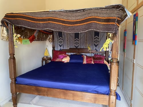 Wooden four-poster canopy bed with blue mattress and decorative fabrics at Le Lama Zébré guesthouse, Penmarch