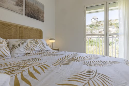 Luminosa habitación mediterránea con ropa de cama estampada en pan de oro, cabecero de ratán y balcón con vista a las montañas en Numidas Open