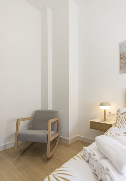 Moderno dormitorio en el Numidas Open House Hotel con mecedora de madera, cama plataforma, lámpara de noche y decoración minimalista
