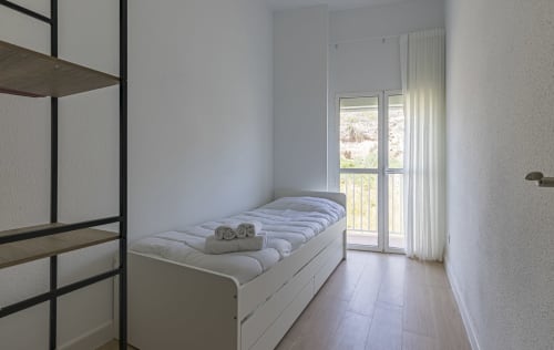 Dormitorio moderno en Numidas Open House Hotel, Murcia con cama blanca, suelo de madera, balcón con vistas a las montañas y