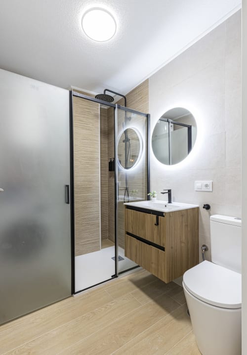 Baño moderno del Numidas Open House Hotel en Murcia con mueble de madera, espejo iluminado y ducha independiente