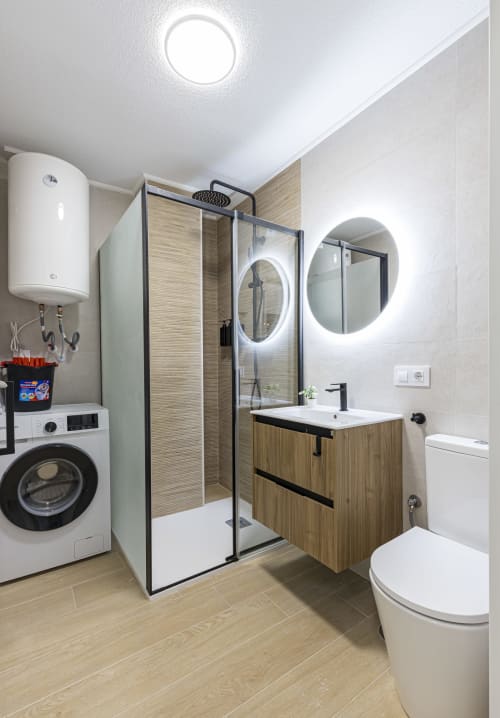 Baño moderno en apartamento del hotel Numidas Open House con ducha, vanity de madera, espejo iluminado, lavadora y