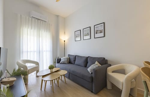Sala moderna del hotel Numidas Open House con sofá gris, sillas color crema, mesas de madera y vistas a la montaña