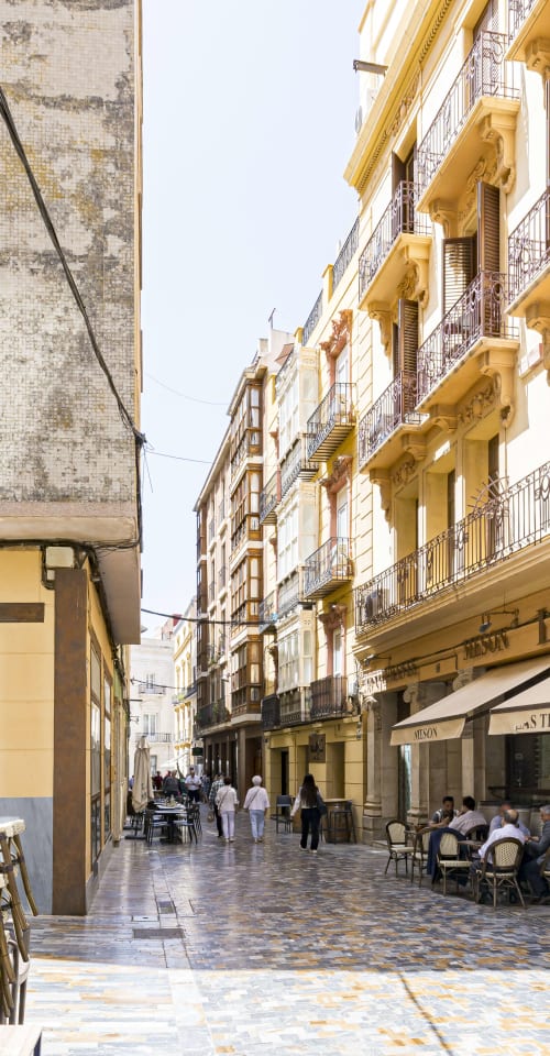Calle estilo mediterráneo en Murcia con edificios amarillos, terraza de café al aire libre y peatones en un encantador europeo
