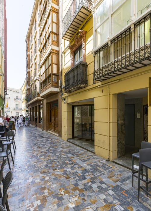 Patio de estilo mediterráneo en Murcia con fachada amarilla, barandillas de hierro decorativo y pavimento de baldosas de terracota