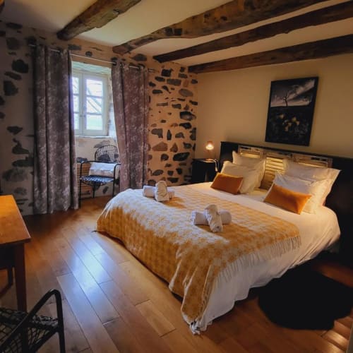 Chambre rustique au Mas De Rigoulac avec poutres apparentes, mur en pierre et literie dorée à Argences-en-Aubrac