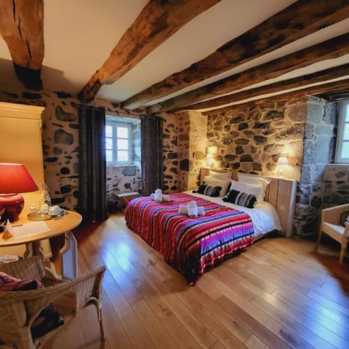 Chambre rustique en pierre du Mas De Rigoulac avec poutres apparentes, literie rayée rouge et éclairage chaud