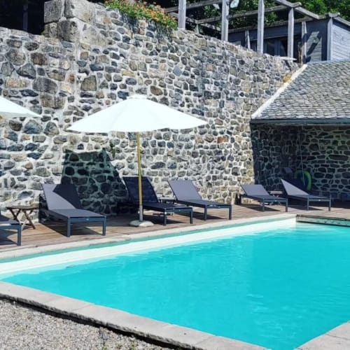 Piscine du Mas de Rigoulac avec eau turquoise, transats, parasol blanc et murs en pierre à Argences-en-Aubrac