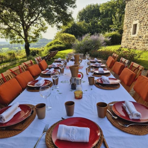 Table de salle à manger extérieure dressée pour les hôtes au Mas De Rigoulac, Argences-en-Aubrac, avec assiettes rouges et chaises aux coussins orange