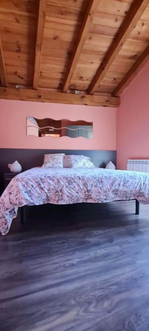 Acogedora habitación en Casas Rurales La Viña con techo de vigas de madera, paredes rosa, ropa de cama estampada y suelos de madera oscura