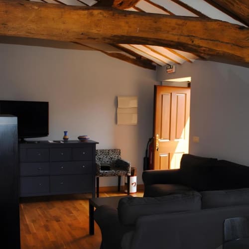 Sala de estar rústica con vigas de madera, muebles negros y puerta naranja en Casas Rurales La Viña