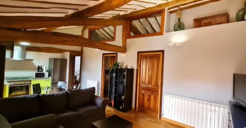 Sala de estar diáfana en apartamento La Viña 2 con vigas de madera, cocina, sofá oscuro y puertas de madera en Casas Rurales