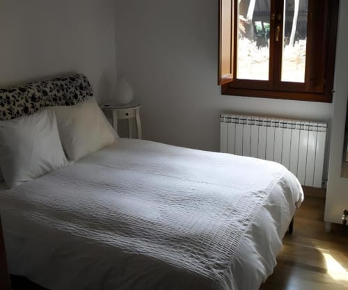 Dormitorio luminoso con ropa de cama blanca, cabecero con estampado negro y ventana de madera en Casas Rurales La Viña