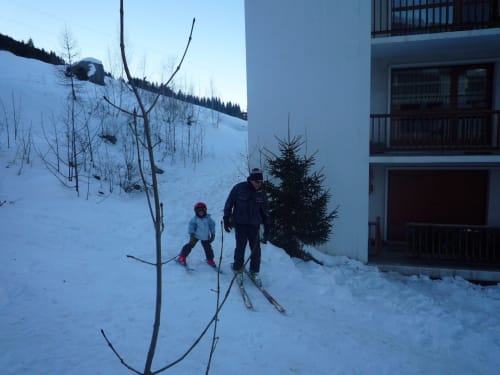 Deux skieurs sur une pente enneigée à côté de l'hôtel Zoppas Courchevel, avec des montagnes boisées en arrière-plan
