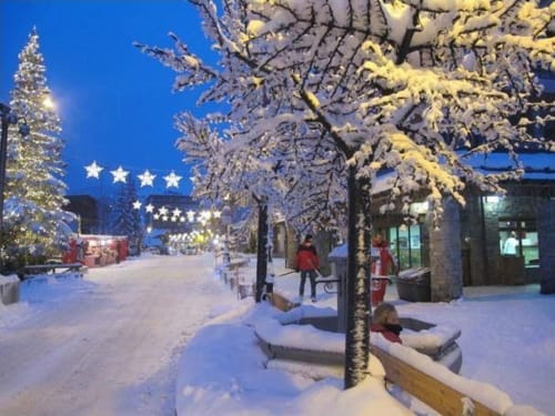 Rue décorée de sapins enneigés et illuminations scintillantes avec sapin de Noël à la tombée de la nuit à Zoppas Courchevel