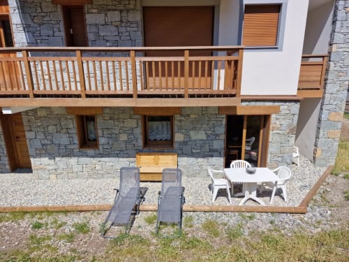 Terrasse Zoppas Courchevel avec façade en pierre, garde-corps en bois, transats et coin repas